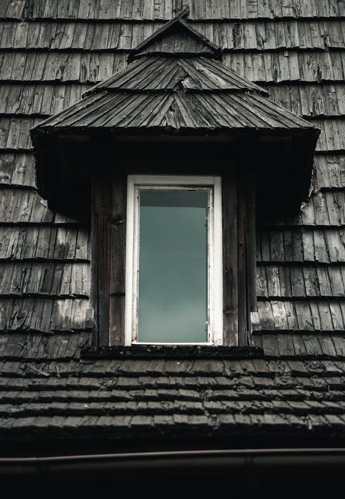 Close-up of an old dormer window with wooden shingles on a traditional roof.