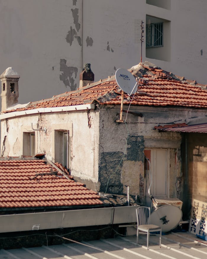 An urban rooftop with red roof tiles, a satellite dish, and a solitary chair.